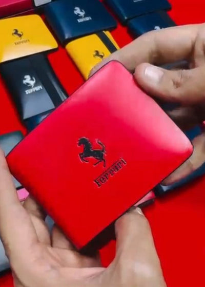 Red wallet with Ferrari logo held by a hand, with other wallets in the background.